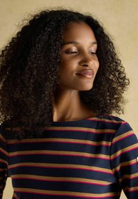 Tumestriibuline topp, millel on horisontaalsete triipudena kuldne ja roosa. Pehme, tekstureeritud kangas, ümar kaelus ja keskmise pikkusega varrukad kergete aktsentidega.