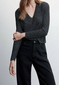 Top lungo con maniche, in tessuto nero con filati metallici, con scollatura a V profonda e design aderente, abbinato a jeans neri a vita alta.