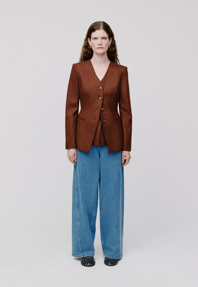 Bruine linnen blazer met notch-lapels, vijf knopen, taillezakken, gecombineerd met wijde blauwe jeans en gestipte zwarte schoenen.