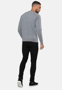 Grå sweater med rund halsudskæring, lange ærmer, ribbede manchetter og kant, parret med sorte skinny jeans og sorte sneakers.