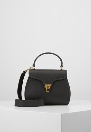 Sac à main en cuir noir avec fermoir doré, poignée supérieure et bandoulière amovible, posé sur un socle blanc sur fond gris.