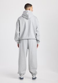 Sweat-shirt gris à capuche, coupe ample et poignets côtelés ; associé à un pantalon de survêtement gris assorti, doté d'une taille élastique et de poignets.