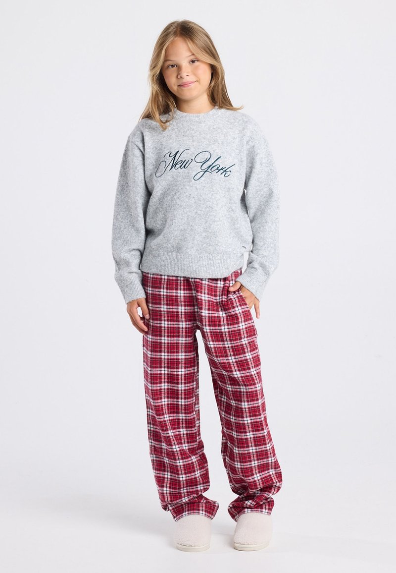 Pull en laine gris avec broderie "New York", associé à un pantalon de pyjama à carreaux rouge et blanc. Le pantalon est ample et a une texture douce.