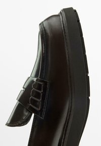 Black leather shoe with a smooth finish, featuring a strap with a buckle detail and a thick, textured sole.