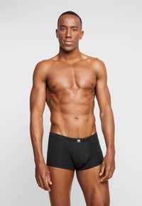 Black boxer shorts made of a smooth, stretchy fabric with a logo on the waistband. The fit is snug, highlighting a muscular physique.