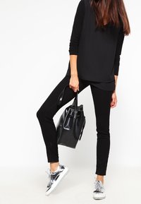 Haut noir à manches longues associé à un pantalon skinny noir et des baskets à lacets argentés. Un sac fourre-tout noir complète la tenue.