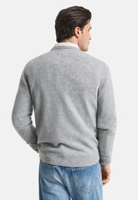 Maglione grigio a maglia con polsini e orlo a coste, caratterizzato da un design colletto classico, indossato sopra jeans in denim blu.