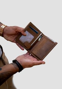 Brown leather wallet opened, featuring card slots, a clear ID pocket, and a zippered compartment. Textured finish, simple design.