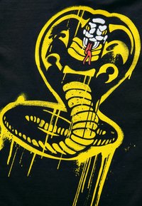 Sort t-shirt med en gul grafik af en sammenrullet kobra med en hvid hoved og en rød tunge, omridset i en spraymalingsstil.
