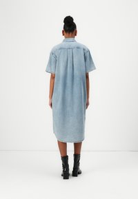Denimklänning med lös passform, korta ärmar och en bakfåll. Ljusblå färg, rundad fåll, tillsammans med svarta ankelskor.