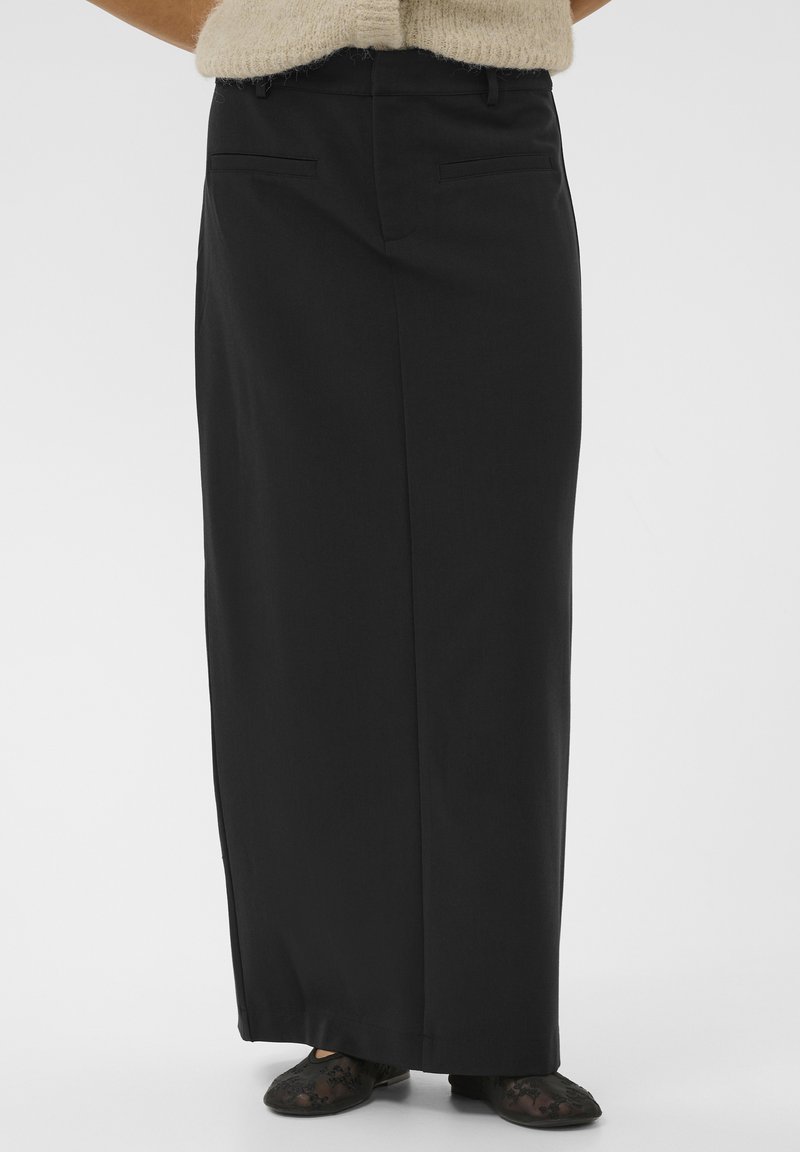 Jupe maxi noire taille haute avec une coupe droite, dotée de deux poches arrière et d'une texture lisse. Assortie avec des ballerines en dentelle noires.