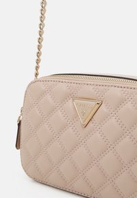 Borsa a tracolla trapuntata color beige con dettagli in oro, caratterizzata da un logo triangolare e una chiusura con zip. Manico a catena attaccato per diverse possibilità di trasporto.