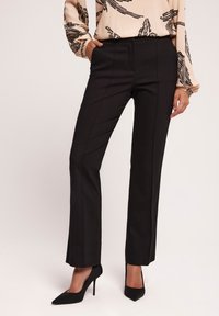 Czarne dopasowane spodnie o prostych nogawkach, z bocznymi kieszeniami i gładką fakturą. W połączeniu z czarnymi szpilkami.