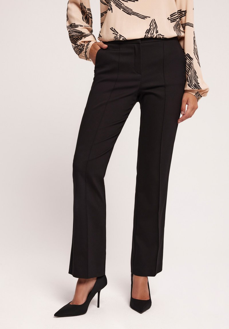 Czarne dopasowane spodnie o prostych nogawkach, z bocznymi kieszeniami i gładką fakturą. W połączeniu z czarnymi szpilkami.
