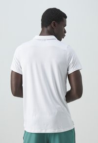 Witte polo met korte mouwen en een platte kraag, met een gladde textuur en een subtiele glans. Achteraan is er een eenvoudig ontwerp te zien.