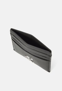 Tarjetero de cuero negro con exterior texturizado, múltiples ranuras para tarjetas y logo en tono plateado en la parte frontal. Diseño de apertura superior.