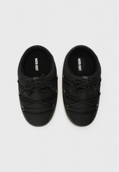 Bottes noires à enfiler avec un dessus en tissu doux, dotées de lacets en élastique entrecroisés, de pompons en fausse fourrure et d'un intérieur rembourré.