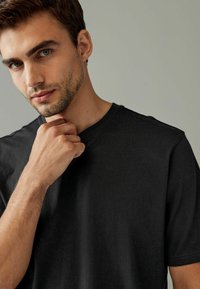Camiseta de algodón negra con diseño de escote en V, mangas cortas y una textura suave. Vista en primer plano de una persona ajustando el cuello.