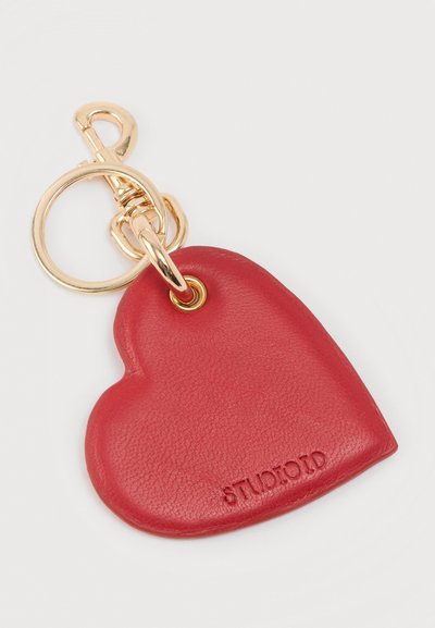 Μπρελόκ σε σχήμα καρδιάς από κόκκινο δέρμα με χρυσό μεταλλικό κρίκο. Διαθέτει χαραγμένο λογότυπο και λείο υλικό.