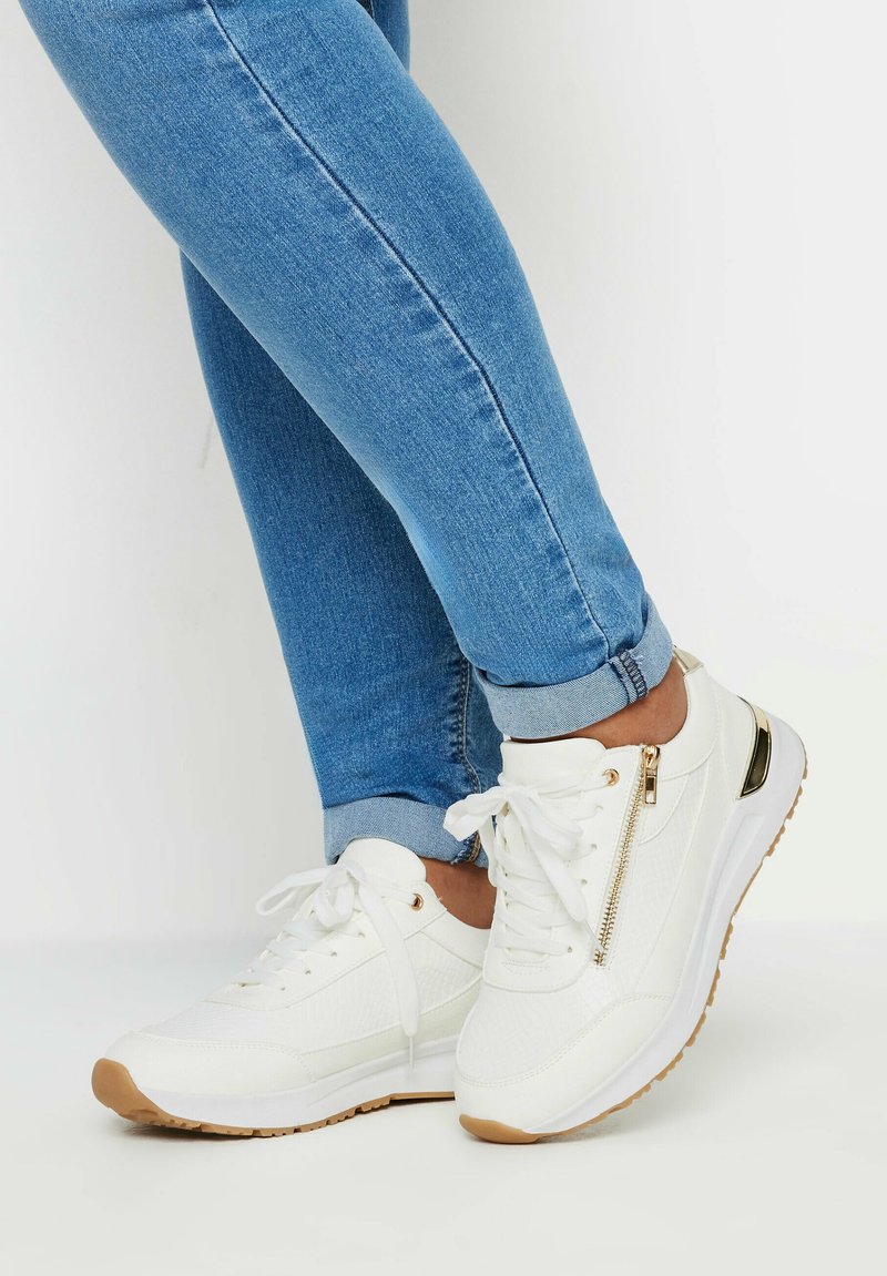 Vita sneakers med texturerad ovandel, guld dragkedjeförsedd detalj och brun gummisula. Matchade med uppvikt blå denimjeans.