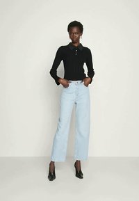 Juoda ilgomis rankovėmis polo marškinėliai su apykakle, derinami su svetimu šviesiai mėlynu aukštu liemeniu plačiomis džinsinėmis kelnėmis ir juodais smailiais kulnais.