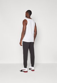 Witte katoenen tanktop, zwarte trainingsbroek en witte sportschoenen met rode accenten. Eenvoudig ontwerp, slim fit stijl, zichtbaar logo op de broek.