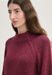 Rippstrickpullover in Burgundy mit hohem Kragen und dezentem Muster, mit lockerer Passform und strukturiertem Stoff, der ein gemütliches Design unterstreicht.