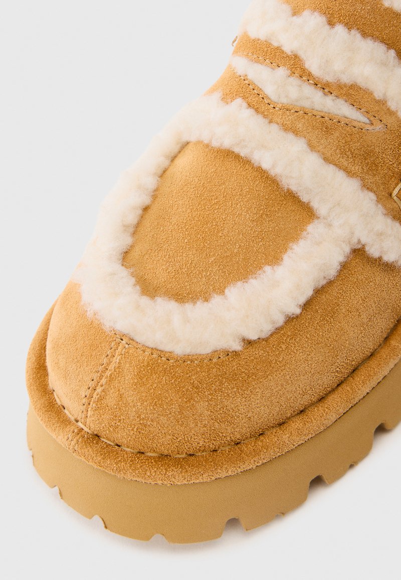 Suede instap schoenen in tan kleur met een voering van schapenvacht en een textuur tan rubberen zool. Kenmerkt gestikte accenten en een ronde neus.