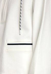 Weißes Sweatshirt mit einer Vordertasche, die einen horizontalen Marineblauen Streifen hat. Enthält eine strukturierte Kapuzenzug mit einem karrierten Muster. Weiches Material.