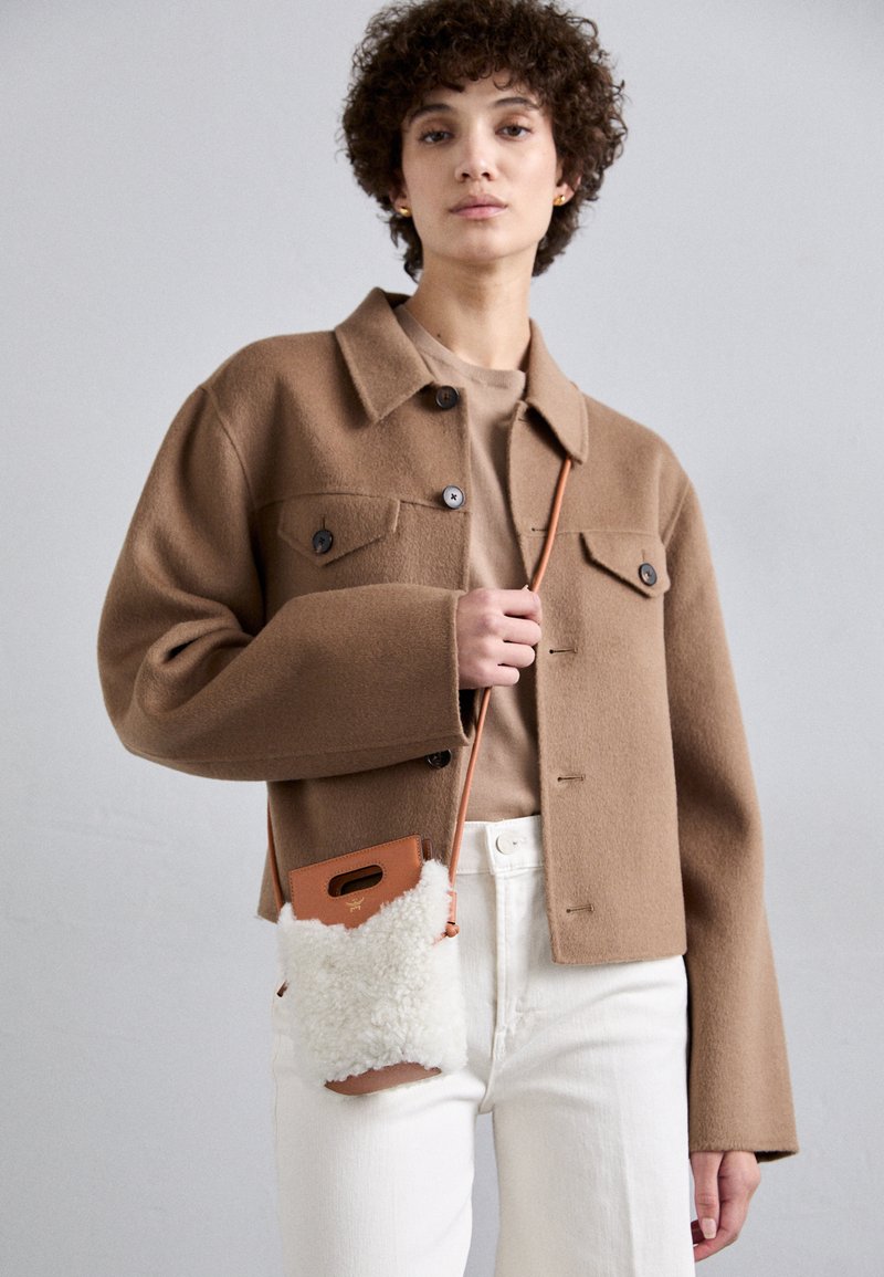 Brun uldblandingsjakke med to forlommer, parret med en sandfarvet top. Hvide jeans og en lille, cremefarvet, shearling crossbody taske.