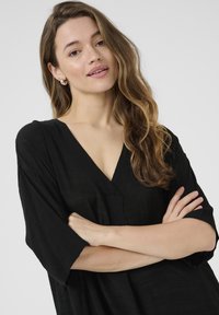 Zwarte V-hals blouse met korte, brede mouwen. Gemaakt van een lichte, gestructureerde stof. Eenvoudig ontwerp met een relaxte pasvorm.