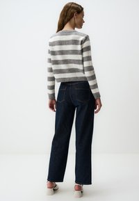 Gestrickter Pullover in Grau und Weiß, aus weichem Material mit rundem Halsausschnitt. Kombiniert mit dunkelblauen, weiten Jeans und weißen Schuhen.