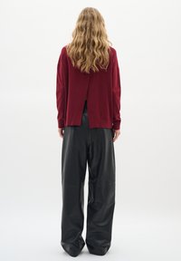 Pull en maille rouge avec une fente dans le dos, associé à un pantalon large en cuir noir taille haute. Texture lisse et coupe décontractée.