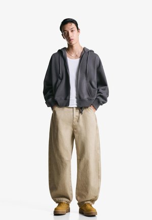 Gray zip-up hoodie with drawstrings, paired with loose beige pants and yellow shoes. Simple, casual design with a relaxed fit.