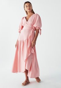 Long pink wrap dress with puff sleeves, a deep V-neck, and a flowing hem. Soft fabric with a tie detail at the waist adds texture.
