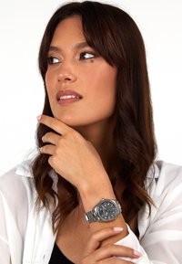 Orologio in acciaio inossidabile argentato con un quadrante nero testurizzato, contrasti di indici delle ore argentati e un bracciale a maglie indossato su un polso.