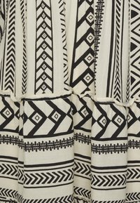 Svartvitt mönstrat tyg med geometriska mönster, inklusive chevronger och diamanter, med en volangkant och texturerat bomullsmaterial.