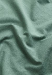 Roheline puuvillane kangas, millel on sile tekstuur, kuvatud voldid ja kortsud, rõhutades selle pehmust ja kerget disaini.