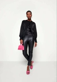Black satin bomber jacket over a black top, paired with shiny black leggings. Accessories include a small pink handbag and pink heeled sandals.