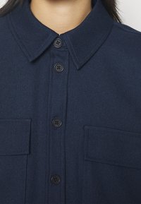 Mörkblå knapp-up skjorta med krage, två framfickor, sex knappar och en strukturerad tyg.