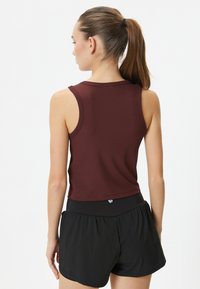 Vinröd ärmlös linne med en figurnära design, kombinerad med svarta shorts. Toppen har en mjuk textur och en enkel rund halsringning.