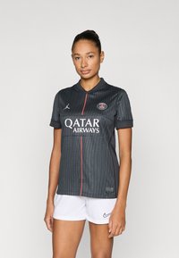 Mustade triipudega jalgpallimängija särk, millel on krae, logo ja valge "Qatar Airways" tekst. Kandmiseks valged püksid ning peen tekstuur.