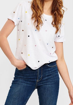 Biała koszulka z krótkim rękawem ozdobiona wielokolorowymi, pastelowymi kropkami, w połączeniu z ciemnoniebieskimi dżinsami.