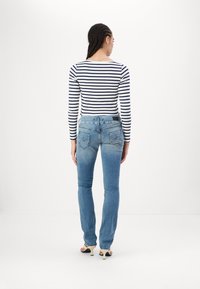 Jean en denim bleu à coupe droite, avec deux poches arrière et un délavage léger. Associé à un haut à manches longues rayé blanc et marine.