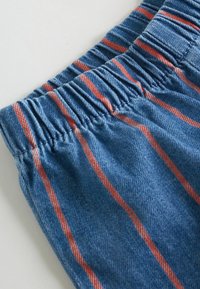 Elastični pojas od plavih traper kratkih hlača s crvenim okomitim prugama; tkanina ima mekanu teksturu i ležeran, opušteni kroj.