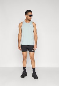 Jasnoniebieska sportowa koszulka bez rękawów z małym logo, czarne sportowe spodenki, czarne skarpetki i czarne buty sportowe. Model stoi na neutralnym tle.