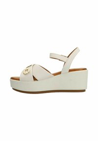 Wedge sandalen met een lichtbeige leren bovenkant, voorzien van kruislings geplaatst banden en een kleine gouden accent aan de voorkant, op een witte platformzool.