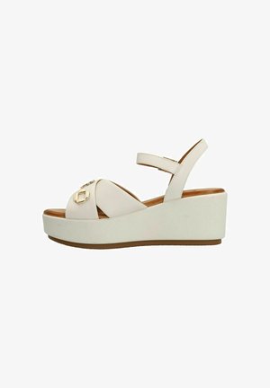 Wedge sandalen met een lichtbeige leren bovenkant, voorzien van kruislings geplaatst banden en een kleine gouden accent aan de voorkant, op een witte platformzool.