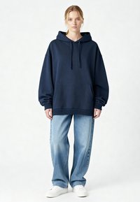 Sweat à capuche surdimensionné bleu marine avec poche avant, poignets et ourlet côtelés ; associé à un jean large bleu clair et des baskets blanches.