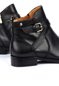 Botas de tobillo de cuero negro con puntera redonda, cremallera lateral, detalle de hebilla y forro beige; acabado texturizado y tacón bajo.